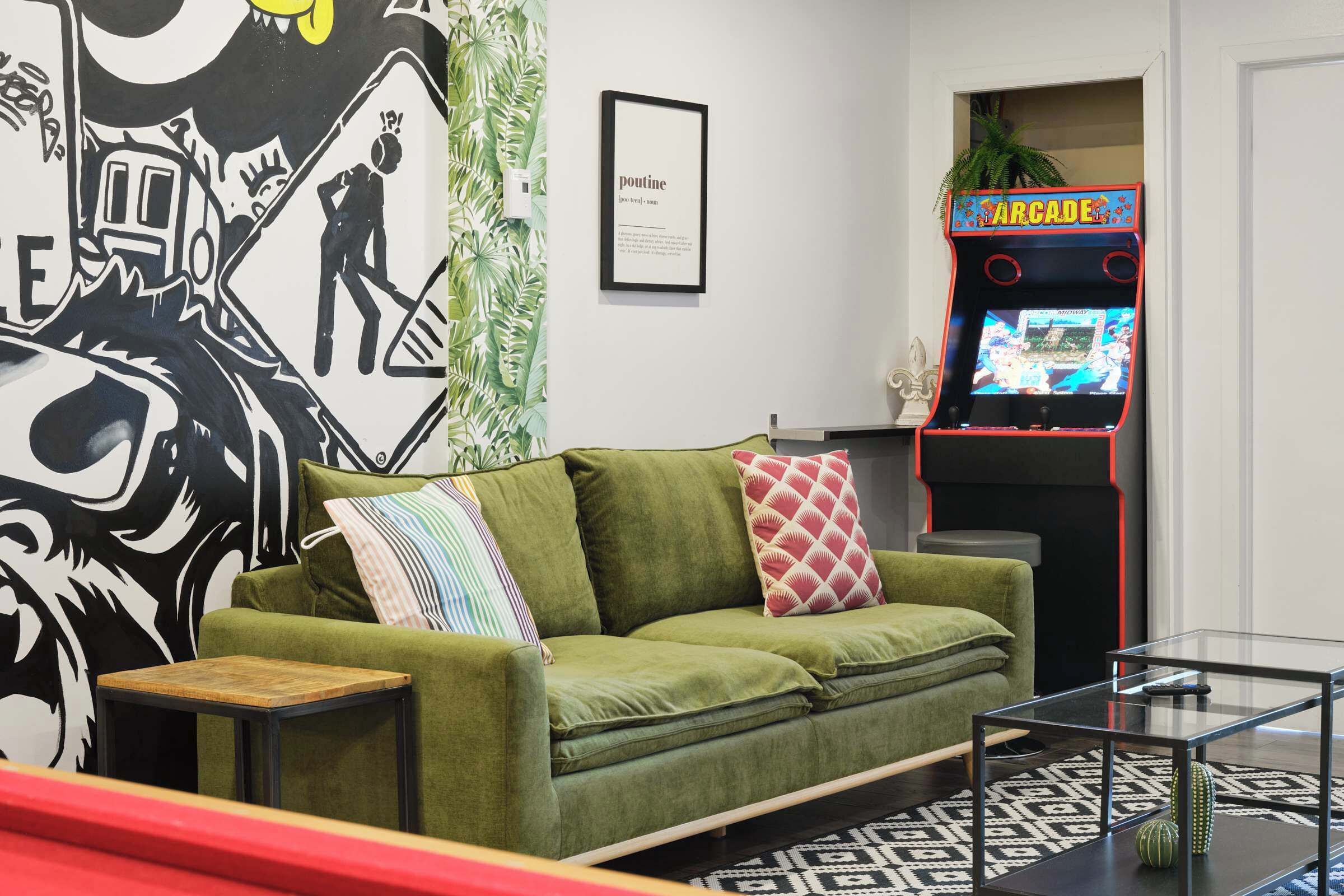 A living room with a green sofa, a small table, a framed picture, and a retro arcade machine.
