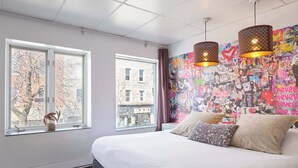A bedroom with a large bed, two windows, and a colorful graffiti wall. - MTLVR #09 | Central Plateau, A/C, Ping-Pong (Montreal)