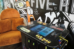 A Pac-Man arcade machine, a brown upholstered chair, and a wall with a large 'FIVE' sign.