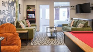 A hotel room with a pool table, two green sofas, a mural, a gaming machine, and a TV. - MTLVR #09 | Central Plateau, A/C, Ping-Pong (Montreal)