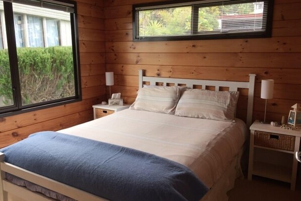 Een slaapkamer met houten lambrisering, een bed, twee nachtkastjes en een raam met jaloezieën.
