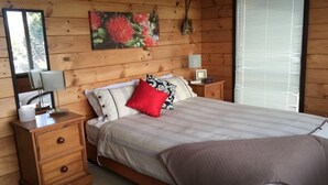 A wooden-paneled bedroom with a bed, nightstands, a lamp, and a painting on the wall. - Paku Paradise, Tairua. (Tairua)