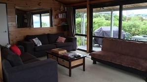 A cozy living room with a sofa, a coffee table, and a bookshelf. - Paku Paradise, Tairua. (Tairua)