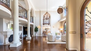 A spacious foyer with high ceilings, a grand chandelier, and a wooden staircase.