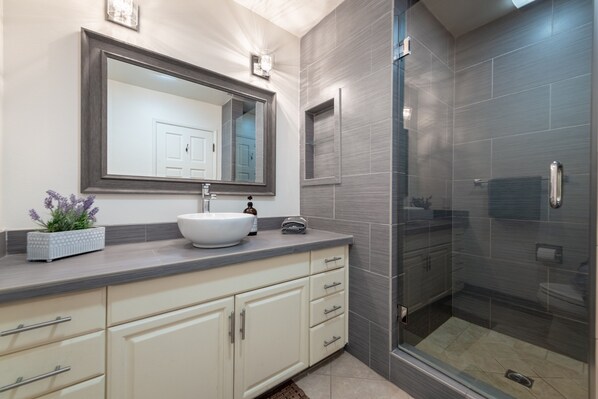 A modern bathroom with a large mirror, a white sink, and a walk-in shower.
