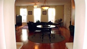 Un espacio abierto que combina sala de estar y comedor, con una mesa redonda y sillas, un sofá y un televisor al fondo.