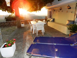 Un patio al aire libre con una mesa, sillas y una butaca azul, además de una planta en maceta.