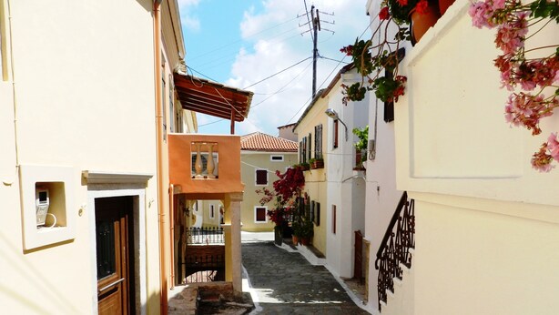 Una estrecha calle adoquinada bordeada por edificios con balcones y macetas con flores.