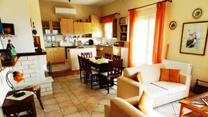Amplia sala de estar con sofá, mesa de comedor y sillas. Se observa una cocina al fondo con armarios y una ventana.
