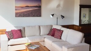 A living room with a white sectional sofa, a wooden coffee table, and a painting of a beach scene. - The Lodge of Stanley (Stanley)