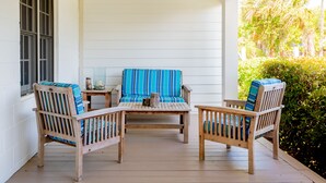 A porch with two wooden chairs and a table, a window, and a view of greenery. - Private Home Located Two Blocks from Restaurants/Shops & 1 Street From Beach! (Folly Beach)