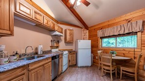 Cocina de cabaña de madera con un lavamanos, estufa, refrigerador y alacenas de madera.