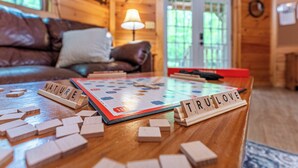 Una mesa de madera con un juego de Scrabble, una lámpara y un sofá en una habitación acogedora con paredes y una puerta de madera.