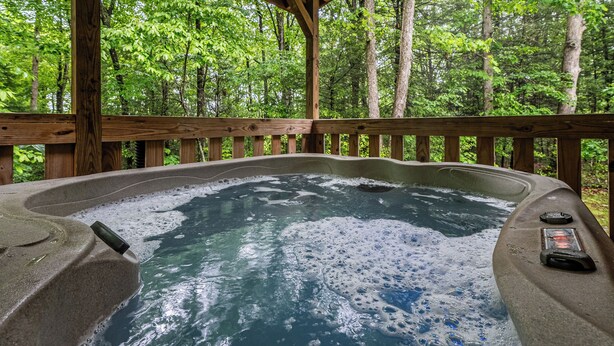 Un jacuzzi rodeado por una terraza de madera, con un bosque al fondo.
