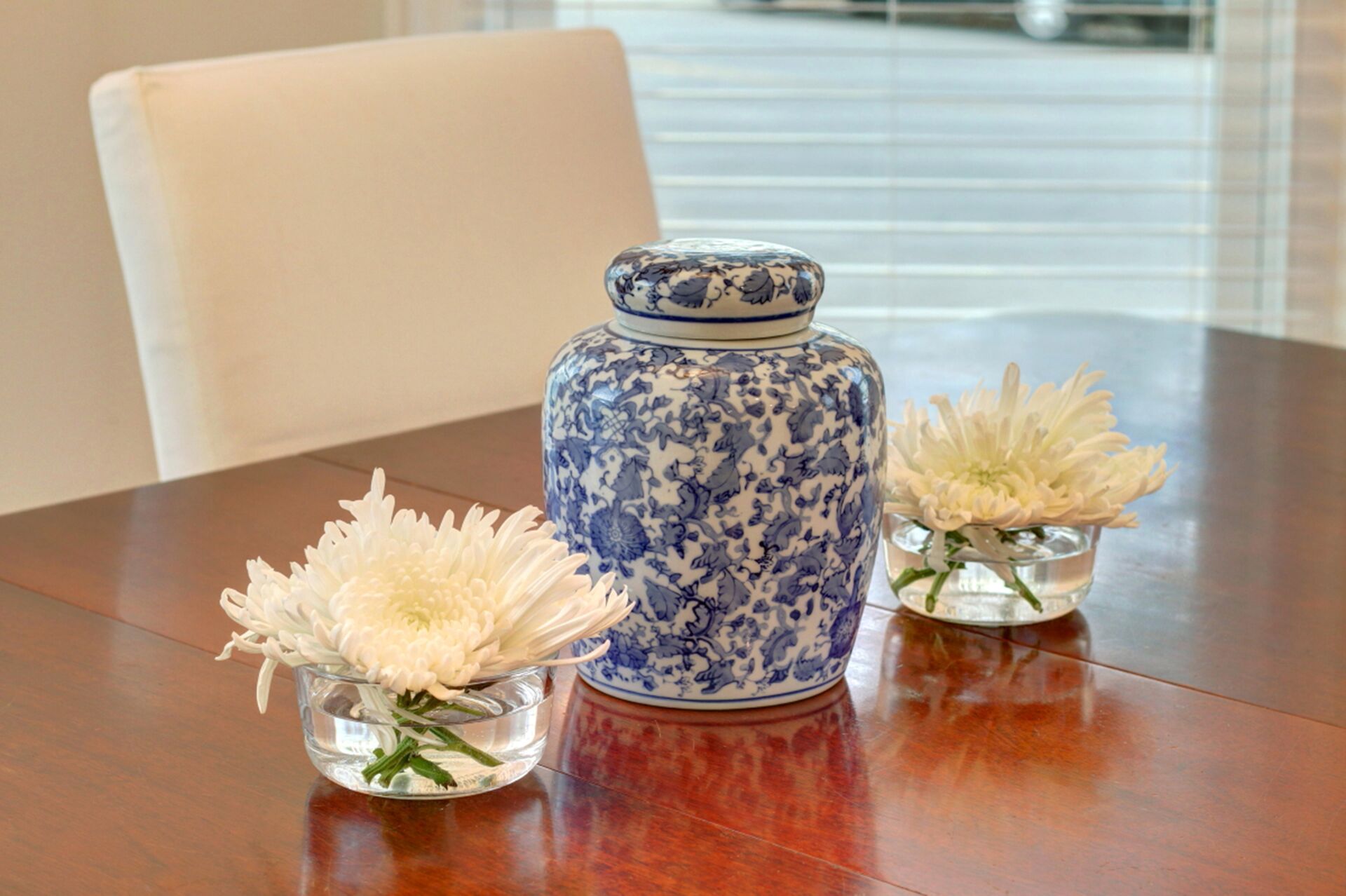 Une table sur laquelle se trouvent un vase en céramique bleu et blanc et deux petits vases en verre contenant des fleurs blanches.