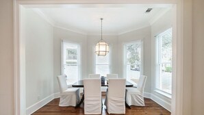 Uma sala de jantar com uma mesa redonda, cadeiras brancas e um lustre.