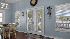 A room with a dining area, a clock on the wall, and a view of the outside through the windows.