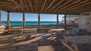 An outdoor wooden deck with picnic tables overlooking a beach.