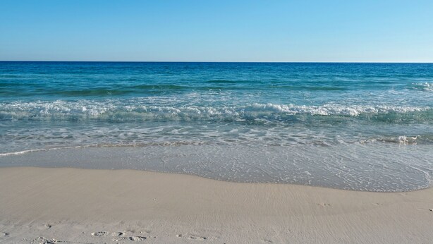 A beach with clear blue water and a sandy shore.