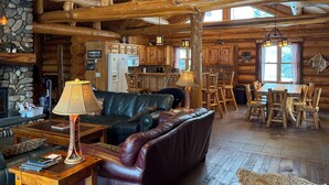 Interior rústico con chimenea de piedra, sofá de cuero, mesa de comedor de madera y una zona de cocina.