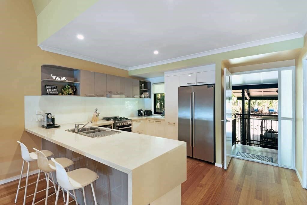 A modern kitchen with a central island, white bar stools, and a stainless steel refrigerator.