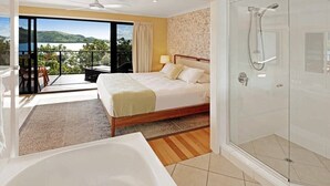 Ein modernes Hotelzimmer mit einem großen Bett, einem eigenen Badezimmer mit Glasdusche und einem Balkon mit Blick auf die Hügel.
