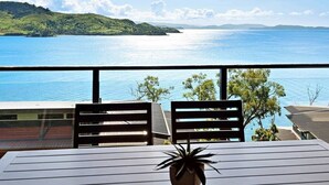 Ein Balkon mit zwei Stühlen und einem Tisch, mit Blick auf ein großes Gewässer und grüne Hügel.
