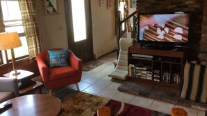 Ein Wohnzimmer mit Fernseher, einem roten Sessel, einem Bücherregal und einer Treppe.