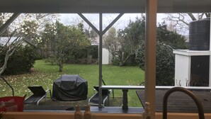 Udsigt fra et vindue over en baghave med grill, bord og springvand.
