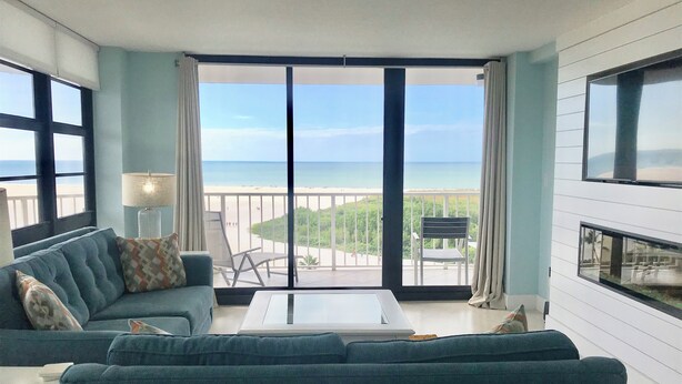 Ein modernes Wohnzimmer mit einer großen Schiebeglasdoor zum Balkon mit Blick auf Strand und Meer.
