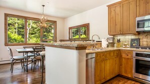 Une cuisine avec des meubles en bois, un four en acier inoxydable et un coin repas comprenant une table et des chaises.