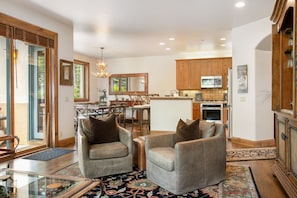 A spacious living room with two leather armchairs, a dining area with a wooden table, and a kitchen with wooden cabinets and modern appliances.