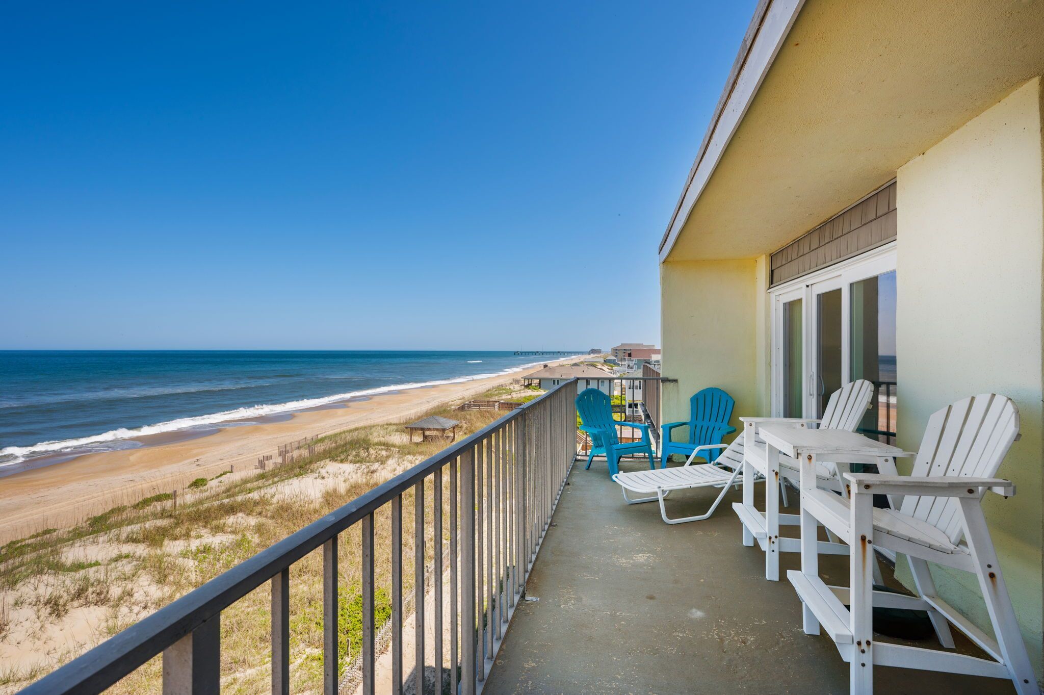 Ein Balkon mit Blick auf Strand und Meer, weiße Stühle und ein Tisch.