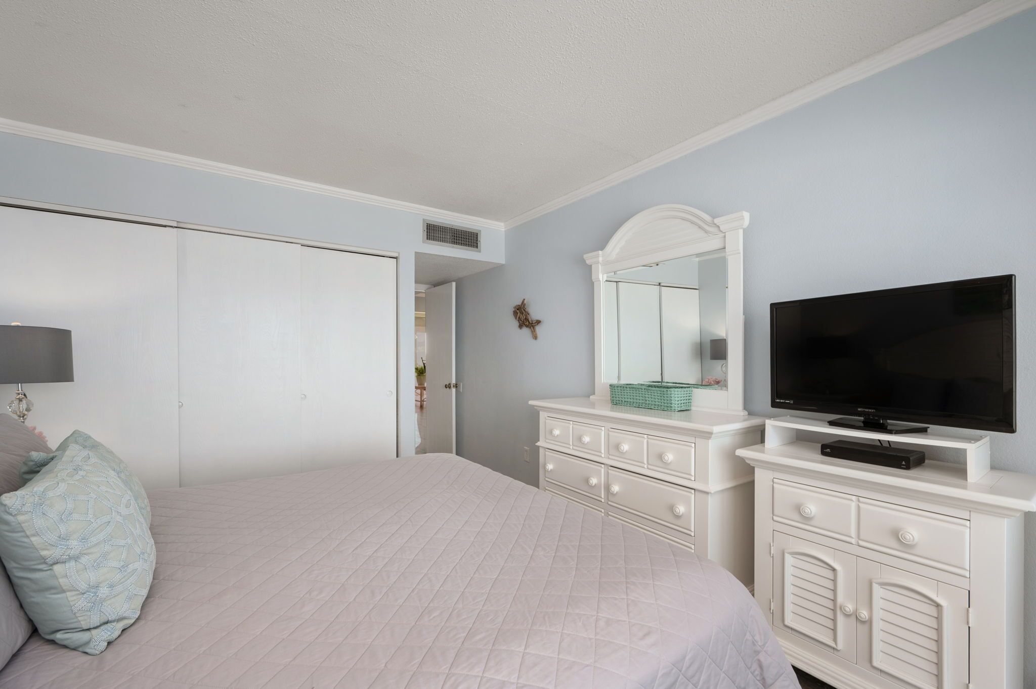 A bedroom with a bed, dresser, TV, and a door.