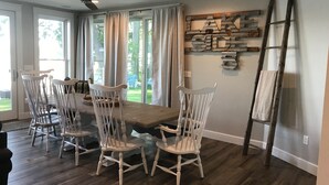 Un coin repas avec une table en bois et quatre chaises blanches, un ventilateur de plafond et une échelle fixée au mur.
