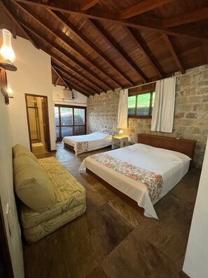 A bedroom with two beds, a sofa, a stone wall, and a wooden ceiling. - Excellent house in Angra with private beach - 10 bedrooms, 8 of which are suites. (Angra dos Reis)