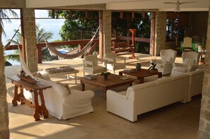 A spacious living area with a large sofa, armchairs, and a wooden coffee table. A hammock is visible outside the window, and the room has a view of the sea. - Excellent house in Angra with private beach - 10 bedrooms, 8 of which are suites. (Angra dos Reis)