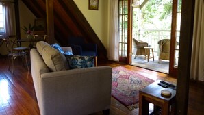Ein gemütliches Wohnzimmer mit einer Couch, Sesseln, einem kleinen Tisch und Blick auf eine Holzterrasse.