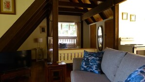 Ein gemütliches Wohnzimmer mit einer Couch, einem Fernseher, einem Holztisch und einem Fenster mit Blick ins Freie.