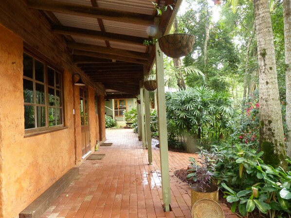 A covered walkway with brick flooring, wooden beams, and hanging planters. - Outback magic in the Hinterland! (Cooroy)