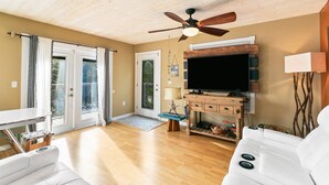 Una sala de estar con ventilador de techo, televisor, un sofá blanco y un mueble de madera.