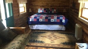 Un dormitorio acogedor tipo cabaña de madera con una cama, una mesita de noche, una silla y un ventanal con cortinas.