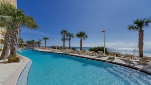 A pool area with lounge chairs and palm trees, surrounded by a building with a clear view of the ocean. - Calypso 6th floor with Gulf Master - Beach Chairs & FREE Activities each day! (Panama City Beach)