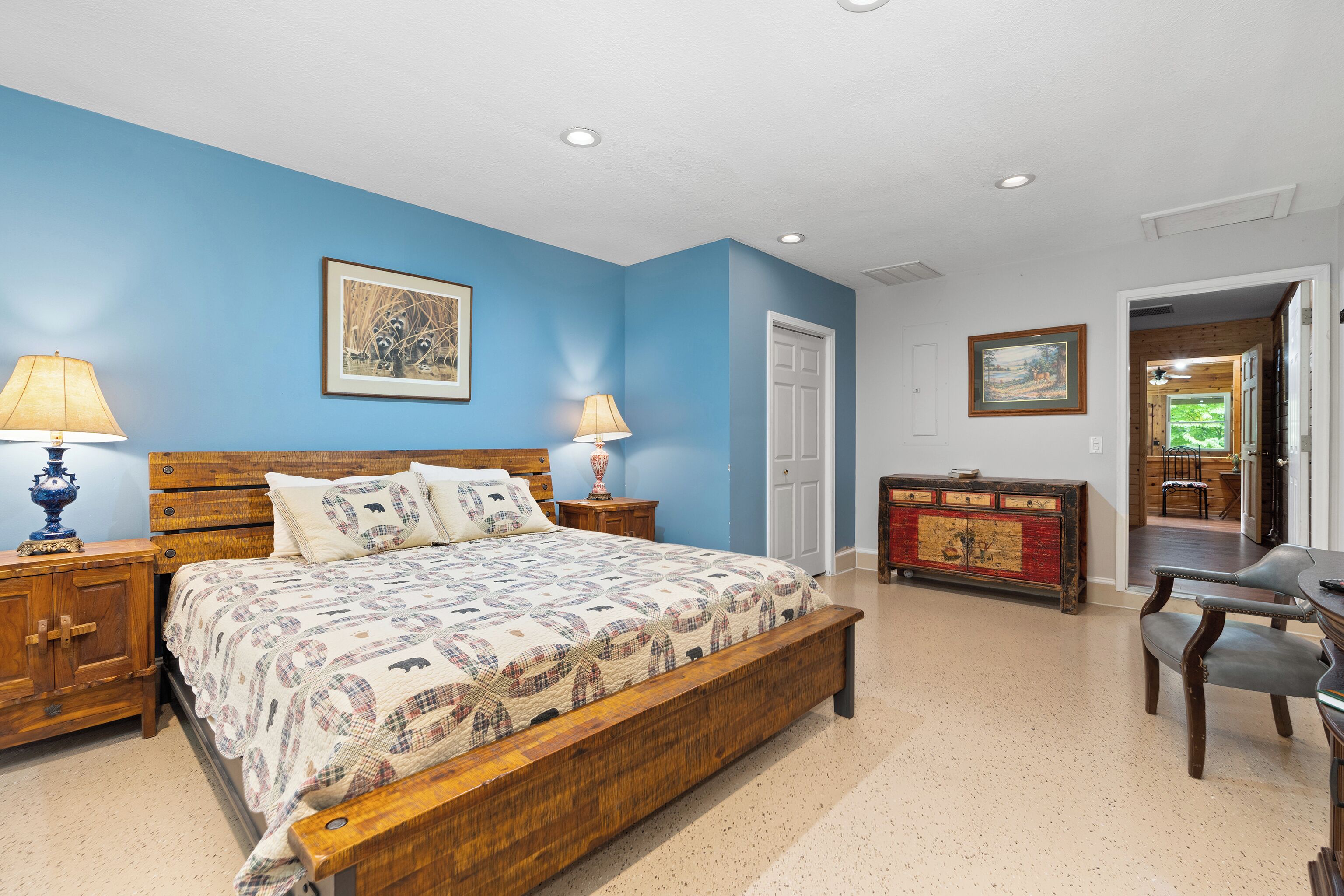 A bedroom with a wooden bed, two bedside lamps, a dresser, and a door leading to another room.