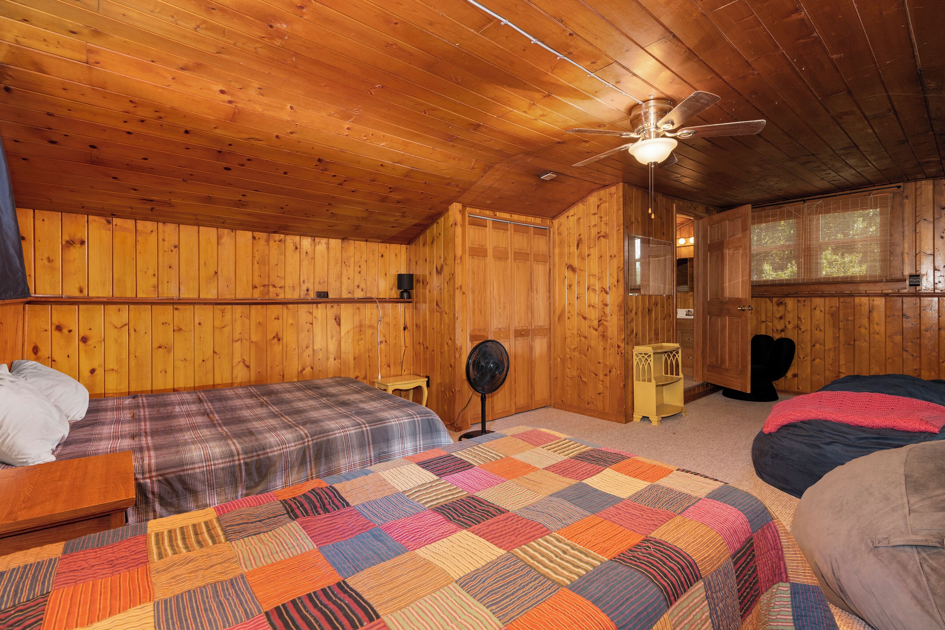 Ein Schlafzimmer einer Holzhütte mit zwei Betten, einem Deckenventilator und einem Fenster.