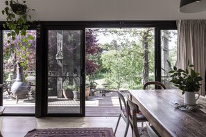 A room with a wooden table, chairs, a rug, and a view of an outdoor patio with plants and a statue.
