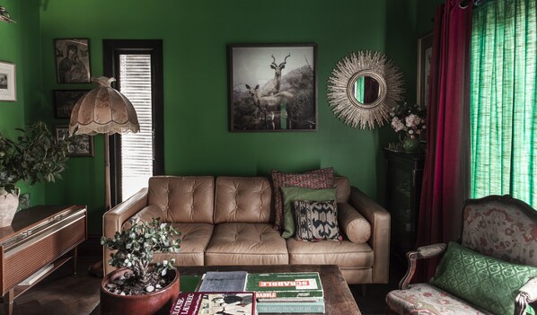 A living room with a green wall, a sofa, a coffee table with books, a lamp, and a decorative mirror.