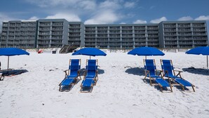 Ein Hotel direkt am Strand mit mehreren Balkonen und einem Strandbereich mit blauen Sonnenschirmen und Liegestühlen.