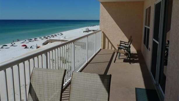 Ein Balkon mit Blick auf einen Strand, ein paar Stühle und ein Tisch.