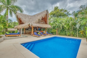 A pool area with lounge chairs and a thatched-roof structure.
